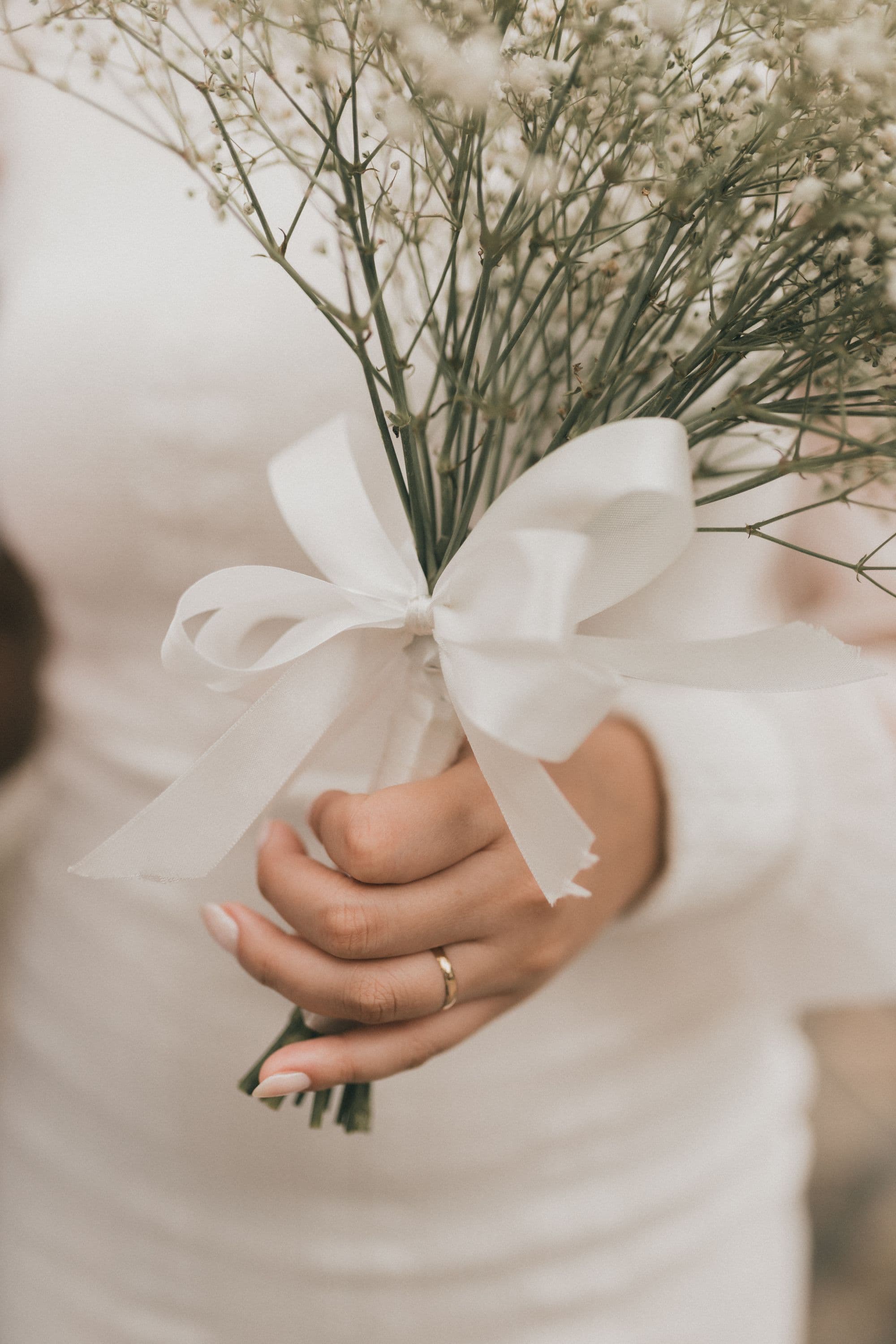 A bride holding a small white bouquet tied with ribbon